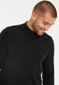 Czarny sweter z golfem z dzianiny z prążkowanym kołnierzem. Dopasowany krój, długie rękawy i miękka tekstura. Brak widocznych wzorów lub detali metalowych.