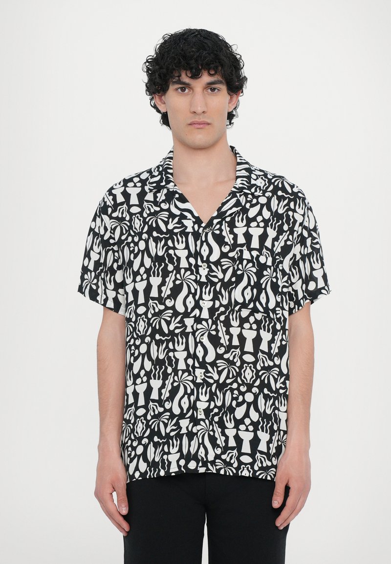 Μαύρο κοντομάνικο πουκάμισο με λευκό αφηρημένο σχέδιο από μαγειρικά σκεύη και σχήματα. Κατασκευασμένο από ελαφρύ ύφασμα με χαλαρή εφαρμογή.