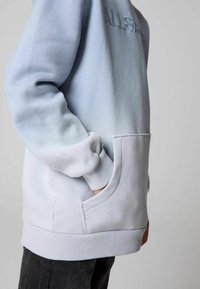 Ljusblå sweatshirt med en gradienteffekt, med en framficka, ribbade ärmslut och en broderad logotyp. Mjuk tygtextur.