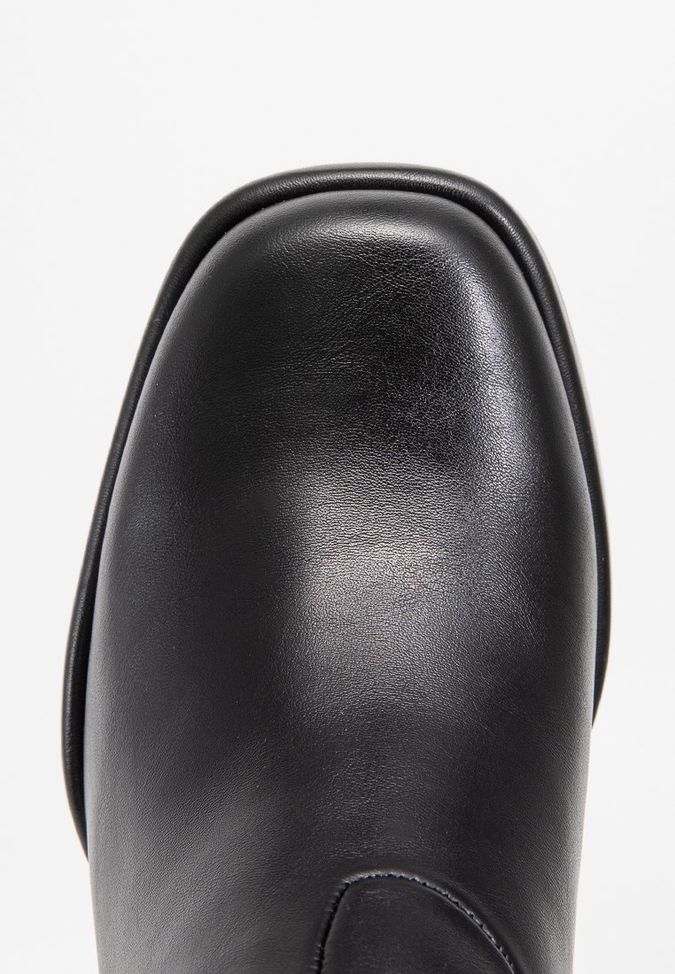 Zwarte leren schoen met een ronde neus, een gladde textuur en een subtiele glans. Heeft een licht verhoogde, gestructureerde zool voor stabiliteit.