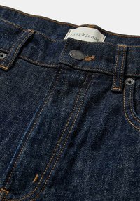Jeans in denim blu scuro con cuciture arancioni, bottone in metallo e rivetti. Presentano un'etichetta con il nome del marchio sulla vita. Tessuto strutturato.