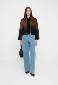 Braune und schwarze Ombre-Cropped-Jacke mit einem Frontreißverschluss, getragen über einem schwarzen Top und hochgeschnittenen blauen Jeans, dazu eine schwarze Handtasche.