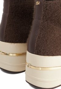 Brown fur and leather ankle boots with a cream platform sole, featuring a gold accent band and logo detail on the side.