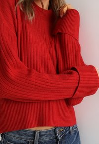 Czerwony sweter z prążkowanego dzianiny z wysokim kołnierzem i szerokimi mankietami. Tkanina jest miękka, z teksturowanym wzorem, o krótkim kroju.