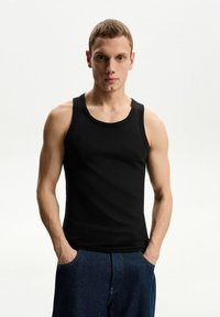 Črn rebrast top s širokimi naramnicami, prilegajoč dizajn in zaobljen ovratnik, v kombinaciji s plavimi jeans kratkimi hlačami. Gladka tekstura.
