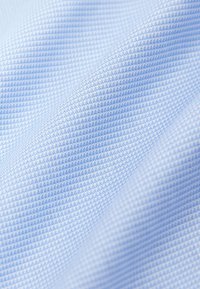 Tissu bleu clair avec un motif quadrillé finement texturé, présenté en gros plan avec des plis doux créant des ombres délicates.