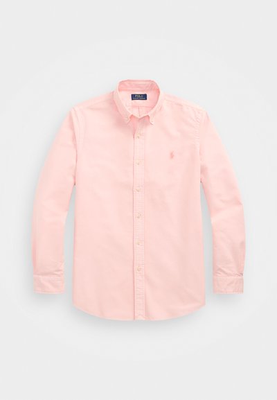 Camisa rosa clara de botão com mangas longas, colarinho e corte clássico. Apresenta um logotipo bordado e um fecho frontal com botões de tonalidade clara.