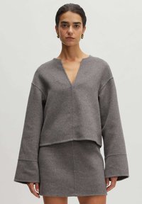 Grauer Wollpullover mit weitem V-Ausschnitt und gekürztem Saum, kombiniert mit einem passenden grauen Rock. Mit weiten Ärmeln und weicher Textur.