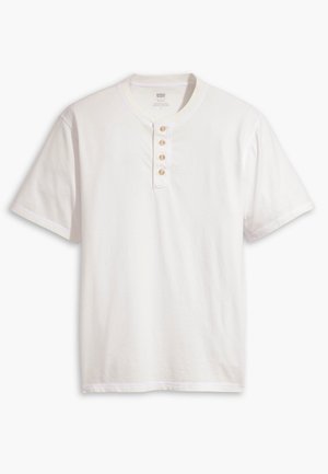 Chemise Henley blanche à manches courtes avec quatre boutons beige et un col rond, présentée sur un fond uni.