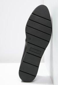 Suola di scarpa in gomma nera con scanalature orizzontali e un motivo testurizzato, caratterizzata da un logo di marca rettangolare nell'area del tallone.
