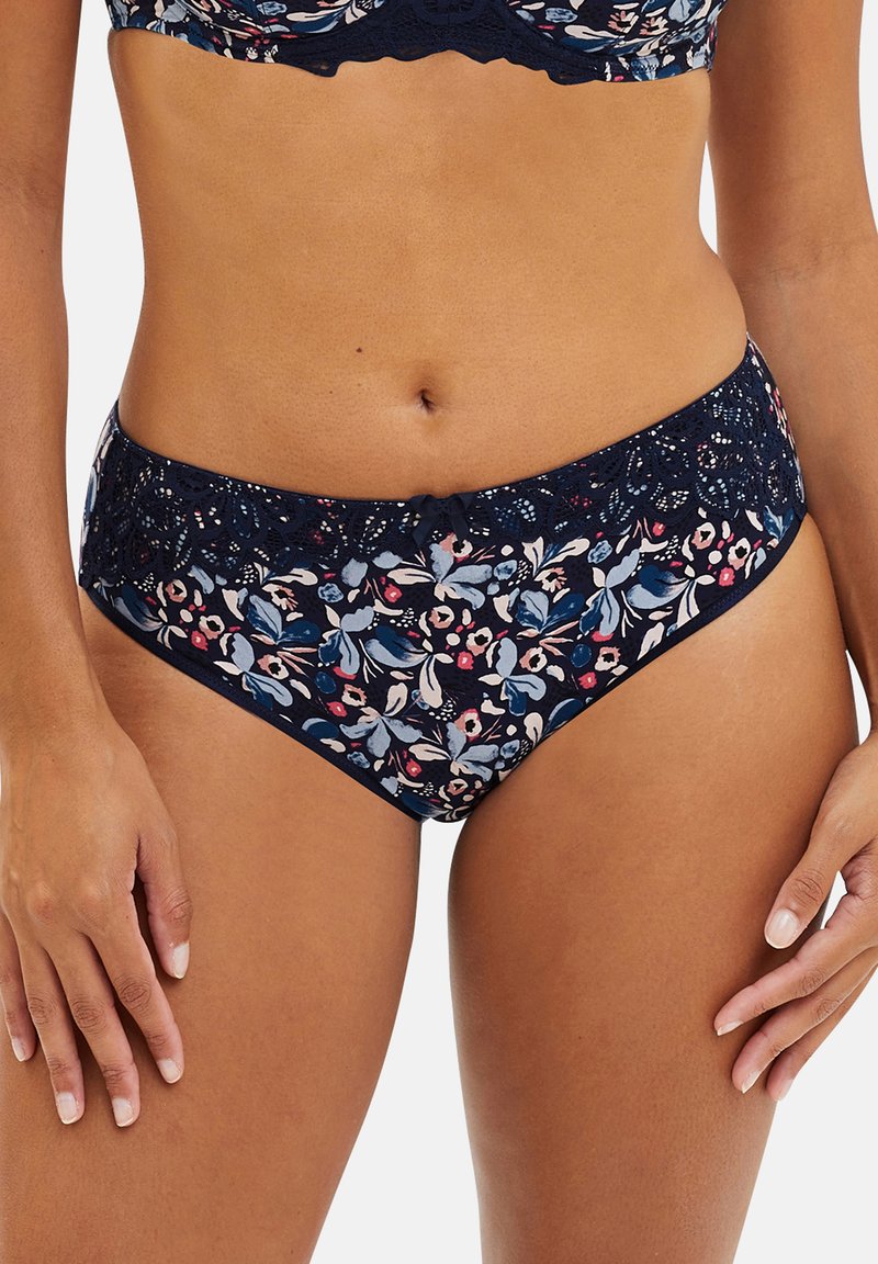 Vrouw in een marineblauwe bloemenbikini met kanten rand en een strikje aan de voorkant, gezien van halverwege de torso tot aan de bovenbenen.