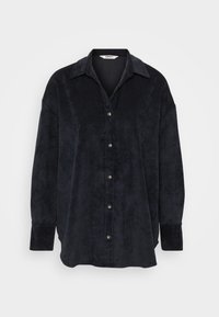 Svart fløyels skjorte med knapper og krage, med myk tekstur, lange ermer og kremfargede knapper langs frontplagget.