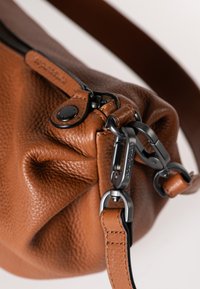 Bruine leren schoudertas met een gestructureerde afwerking, voorzien van een zwarte rits en metalen hardware. Verstelbare schouderriem bevestigd met clips.