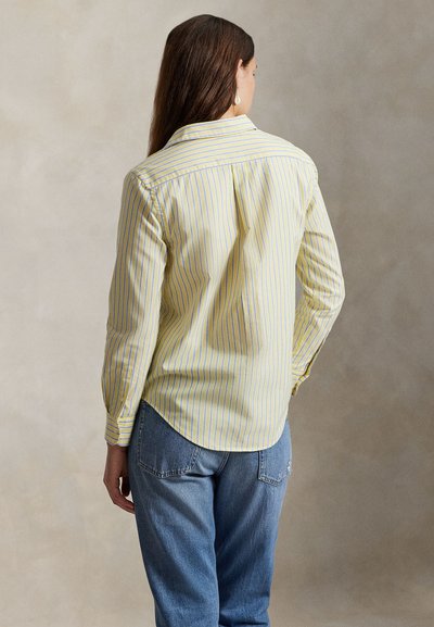 Κίτρινο και μπλε ριγέ πουκάμισο με μακριά μανίκια, γιακά με κουμπιά και καμπύλη τελειώματα, συνδυασμένο με ανοιχτόχρωμο μπλε τζιν.