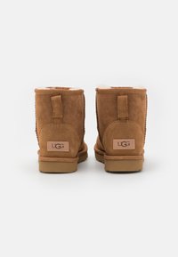Stivaletti ankle in suede marrone con fodera morbida, dotati di una linguetta posteriore e di etichetta con marchio, suole piatte e dettagli di cucitura a vista.