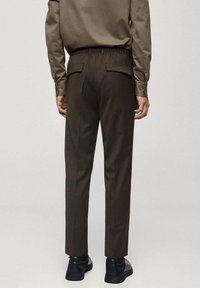Brune bukser med elastisk waistband, der har to baglommer, skræddersyet design og lige benpasform, parret med sorte sko.