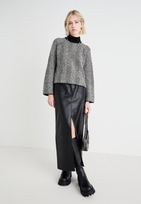 Svart og hvitt houndstooth strikkegenser med senkede skuldre, kombinert med et sort skinnskjørt med høy splitt og kraftige svarte støvler.