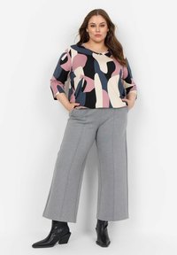 Top a maniche lunghe multicolore a motivi in rosa, blu e nero, abbinato a pantaloni grigi a gamba larga e stivaletti neri con punta affilata.
