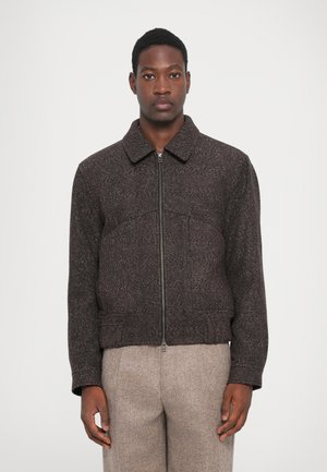Dark brown zip-up jacket, textured fabric, collared design, fitted waist, with subtle detailing and long sleeves, paired with light trousers.
