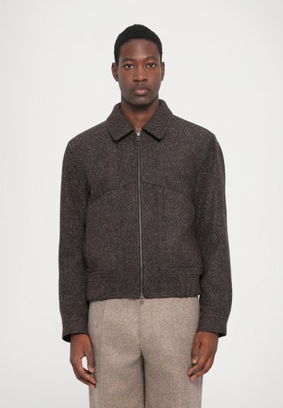 Dark brown zip-up jacket, textured fabric, collared design, fitted waist, with subtle detailing and long sleeves, paired with light trousers.