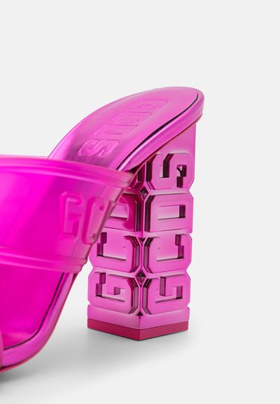 Lyserøde transparente hælesandaler med en robust blokhæl, der har et geometrisk mønster og præget branding på remmen og hælen.
