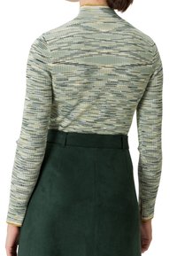 Pitkähihaista puseroa, jossa on teksturoitu vihreä ja beige kuvio, on yhdistetty tummanvihreään nubukihameeseen. Kankaan pinta on sileä ja malli istuva.