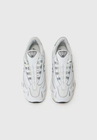 Baskets de sport blanches avec une tige synthétique texturée, présentant un design à lacets, un col rembourré et des accents argentés. Semelle en caoutchouc.