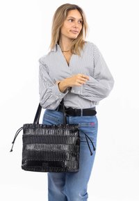Zwart gestreepte handtas met een gestructureerde afwerking, bovenhandvatten en trekkoordsluitingen. Draagt bij een gestreepte blouse en blauwe jeans.