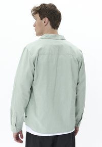 Light green long-sleeve shirt with a relaxed fit, button cuffs, and a fold-down collar. Smooth fabric texture, minimal detailing on back.