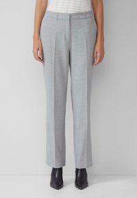 Pantalons gris clair avec un design ajusté, devant plissé et jambes droites. Le tissu semble lisse avec un motif subtil. Portés avec des bottines noires.