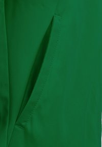 Tessuto verde con una trama liscia presenta una tasca laterale; le cuciture sono visibili lungo la cucitura della tasca, evidenziando durata e design.