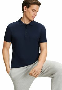 Granatowa koszulka polo z krótkimi rękawami i zapięciem na trzy guziki, w połączeniu z jasnoszarymi dresami. Gładka textura i dopasowany krój.