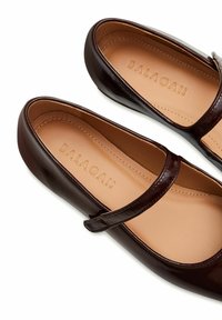 Ballerine in vernice marrone con cinturino alla Mary Jane, caratterizzate da una superficie liscia e con la scritta "BALAGAN" impressa sulla soletta.