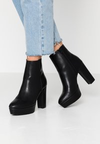 Black leather ankle boots with a chunky heel and platform, featuring a side zipper and smooth texture. Worn with light blue cropped jeans.
