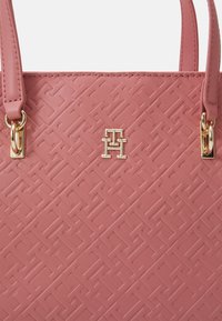Pink textured tote bag made of synthetic material with gold hardware. Features a logo accent and a geometric pattern embossed on the surface.