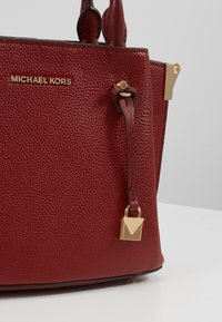 Sac à main Michael Kors en cuir texturé rouge profond avec logo doré et breloque cadenas dorée suspendue à une sangle.