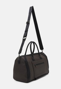 Sac de voyage brun à motif avec des accents noirs, poignées doubles et une bandoulière réglable. Poche avant zippée et détails en matériel brillant.