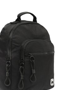 Černý batoh se odolnou tkaninou, zakřiveným vrchem, několika zipovými kapsami s černými úchyty a malým logem na přední straně.