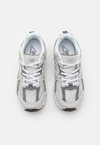 Baskets de sport blanches et grises avec des panneaux en maille, des accents texturés, des détails réfléchissants et des lacets blancs. Semelle noire antidérapante.