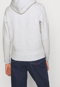 Grau pullover Hoodie mit großer Kapuze, gerippten Bündchen und Saum. Hergestellt aus weichem Gewebe mit glatter Textur, kombiniert mit dunkelblauer Denim.