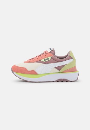 Low-profile Puma sneaker with beige mesh, coral suede overlays, white logo stripe, lime green accents, and thick white sole on gray background.