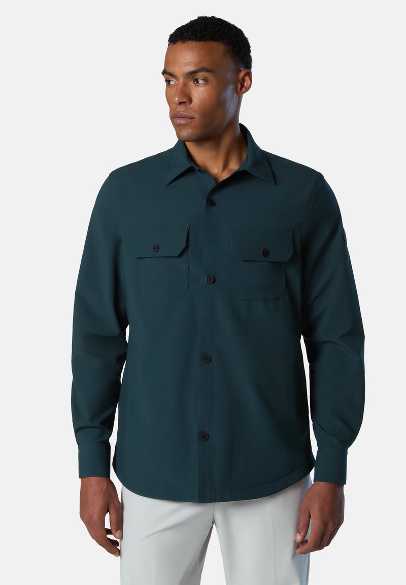 Camisa de manga larga en verde azulado oscuro con cuello abotonado, dos bolsillos en el pecho y un corte relajado. Tejido suave con un ligero brillo.