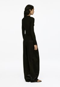 Schwarzes, figurbetontes Langarmshirt kombiniert mit lockeren schwarzen Hosen, die eine glatte Textur und ein minimalistisches Design aufweisen.