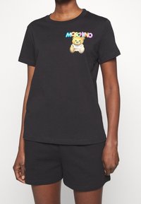 T-shirt nera a maniche corte in cotone, con una grafica colorata di un orso e il logo "Moschino" sul petto. Vestibilità casual.