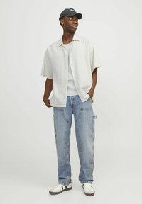 Afslappet outfit med en lys kortærmet skjorte, hvid tanktop, slidte blå cargo-jeans og en sort kasket med logo.