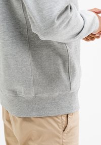 Grijze sweatshirt met geribbelde textuur, elastische manchetten en zoom. Voorzien van zijzakken. Gepaard met lichtbruine broek.