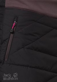 Černá a tmavě hnědá zateplená bunda s prošitím do diamantu, zipovou kapsou s růžovou táhlem a hladkou texturou látky.