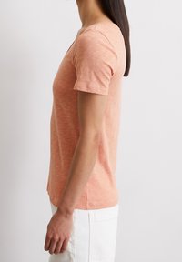 T-shirt a maniche corte di colore pesca realizzato in un tessuto morbido e testurizzato, con un classico collo rotondo e un design slim fit.