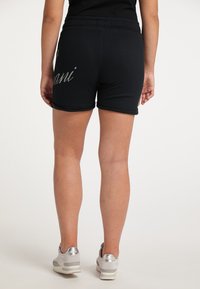 Svarta shorts med silverdetaljer i skrift, gjorda av mjukt material, med en elastisk midja och uppvikt nederkant. Bärs med skor med metalliska accenter.