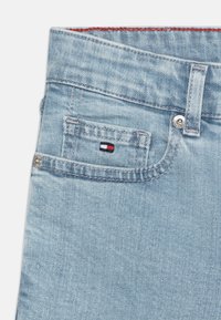 Los jeans de mezclilla de color azul claro presentan un bolsillo frontal con un pequeño parche de logo en rojo, blanco y azul, y un contraste de costuras en naranja.